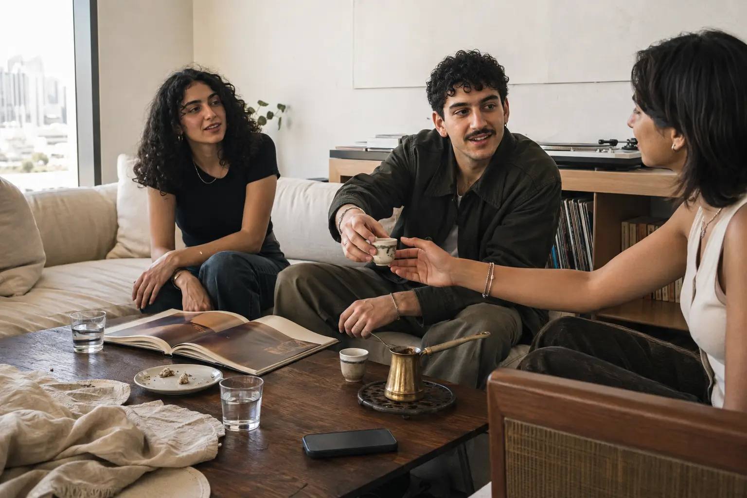 Friends sitting around a low table, passing a small cup of coffee between them.
